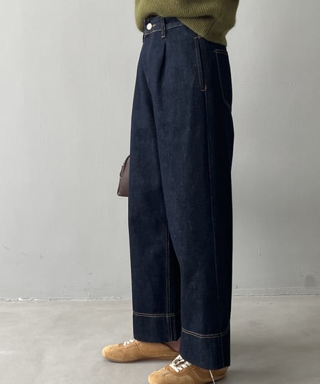 ダークインディゴのワイドデニムパンツを斜めから撮影。太めのストレートラインと裾の切り替えステッチが際立つ。