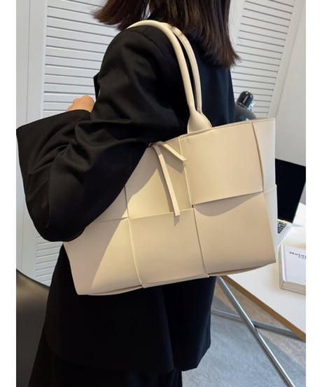 ホワイトの編み込みデザインのトートバッグを肩掛けしている写真。