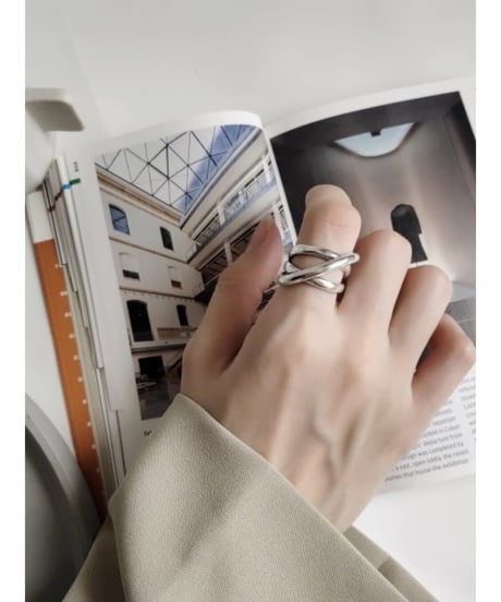 女性の指に着用された、複数のラインがクロスしたデザインの幅広なシルバーリング。袖はベージュのジャケット。