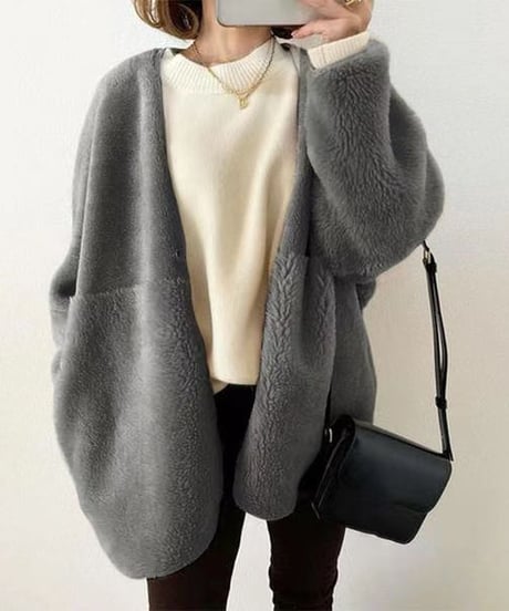白のニットと黒のパンツに、グレーのもこもことした素材のノーカラーカーディガンを羽織った女性のクローズアップ。