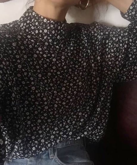 小花柄の黒いハイネックブラウスとジーンズを着用した女性のクローズアップ。
