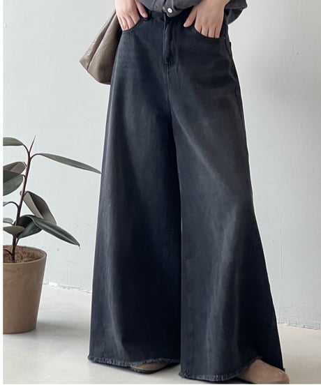 黒の超ワイドデニムパンツとグレーのトップスを着用し、手をポケットに入れた女性の全身。