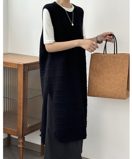 黒のロング丈透かし編みニットベストに白の半袖Tシャツを重ね着した女性の上半身。シルバーのネックレスを着用し、茶色のバッグを持っている。