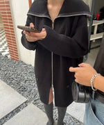 ブラックのオーバーサイズハーフジップニットカーディガンを着用し、スマホを持っている女性の屋外での全身。