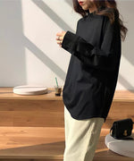 黒のゆったりとした長袖Tシャツ（カットソー）を着用し、ベージュのパンツと黒のスクエアトゥブーツを合わせた女性。カフェのような木目の階段状の空間で立っている。