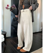 アイボリーの太畝コーデュロイワイドパンツを着用し、手に花束とバッグを持った女性の、ウエストから下のクローズアップ。共布のベルトがポイント。