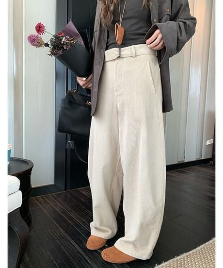 アイボリーの太畝コーデュロイワイドパンツを着用し、手に花束とバッグを持った女性の、ウエストから下のクローズアップ。共布のベルトがポイント。