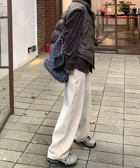 太畝のアイボリーのワイドコーデュロイパンツを着用した女性の全身コーディネート。茶色のダウンベストとシャツを合わせたスタイルを横から見た写真。