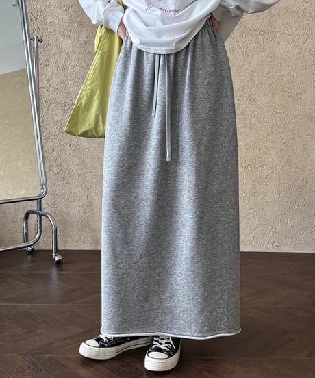 杢グレーのスウェット素材のロングスカートと白いTシャツをきた人物が、スニーカーを履いている下半身ショット。ウエストのドローコードが見える。