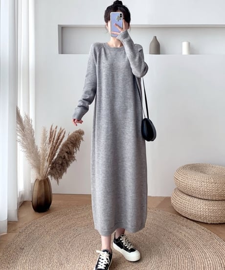 グレーの長袖ニットワンピースを着用し、黒いショルダーバッグをかけている女性の全身。