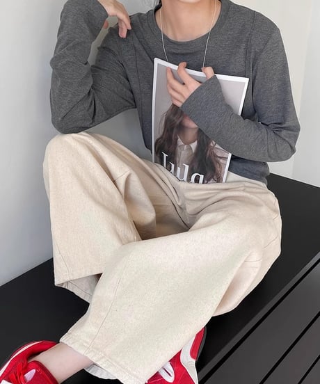 オフホワイトのワイドパンツとチャコールグレーの長袖Tシャツを着て雑誌を手に持った女性が座っている写真。