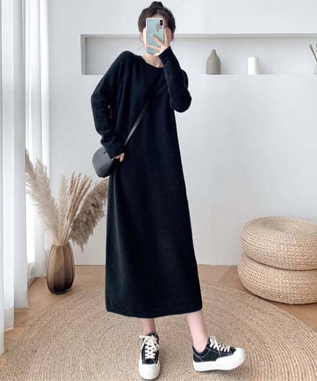 黒い長袖ニットワンピースを着用し、黒いショルダーバッグをかけた女性の全身。