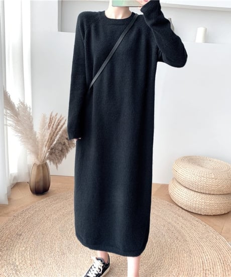 黒い長袖ニットワンピースを着用し、黒いショルダーバッグをかけた女性の全身。