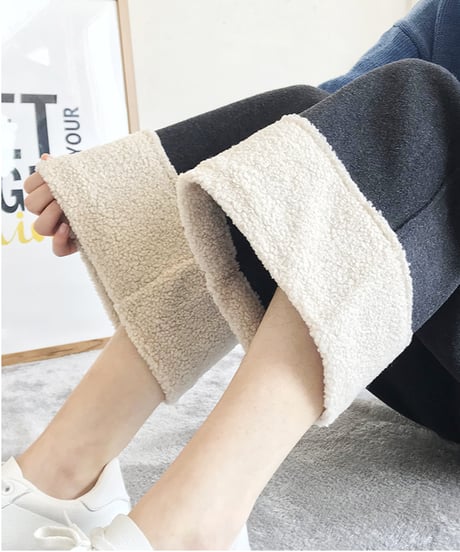 黒のワイドパンツを着用した女性の、膝下から足元を捉えた画像。裾を折り返してオフホワイトのボア（フリース）素材を見せており、上には青いカーディガンを羽織り、足元は白いスニーカーを履いている。
