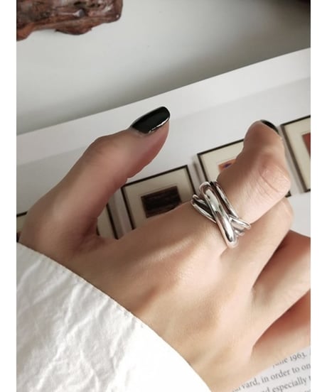 女性の指に着用された、複数のラインがクロスしたデザインの幅広なシルバーリング。指先は黒いネイルで、袖は白いシャツ。