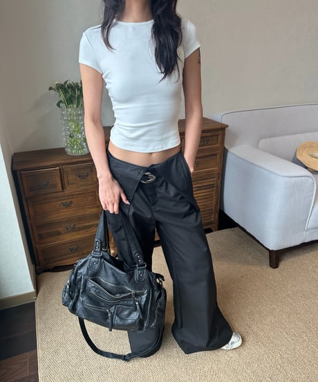 ホワイトTシャツとブラックのワイドレッグパンツを合わせた女性が黒いバッグを持って立っている。