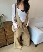 ホワイトの薄手ニットとカーキのオーバーオールパンツを合わせた女性が室内でポーズをとっている。