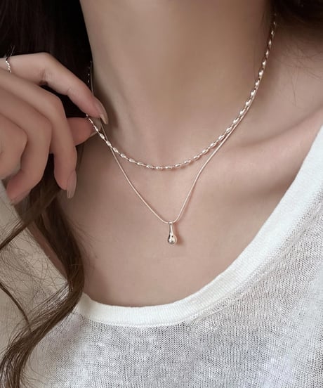 白い服を着た女性の首元に着用された、しずく型チャーム付きのシルバー二連ネックレスのクローズアップ。