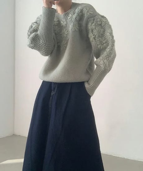 グリーンのフローラル刺繍セーターとスカートをコーディネートした女性、立体感のある編み込みの袖。