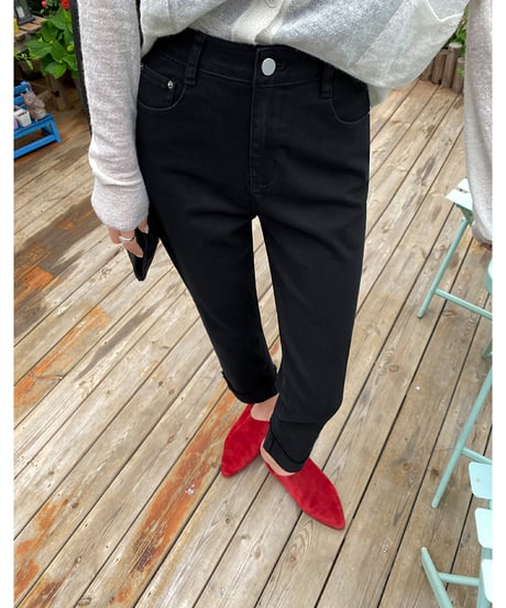 屋外のカフェ風の場所で、黒の裾カフス付きストレートパンツを着用した女性が白いカーディガンと赤のスエード調ミュールを合わせている。