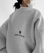 グレーのオーバーサイズスウェットを着用してマスクをした女性の背中側。小さな「M」ロゴと「SERIES OF MINIMALISM」の英文プリントが施されている。
