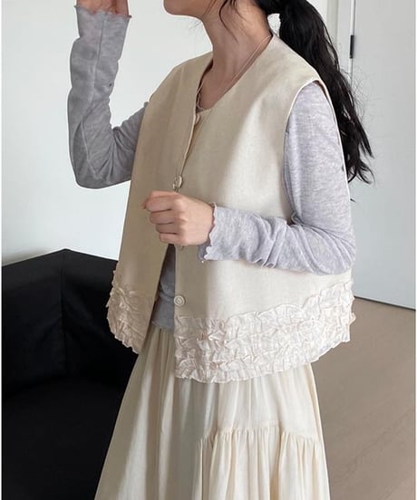 アプリコットのフリル付きベストを着た女性、長袖トップスとスカートにコーディネート。