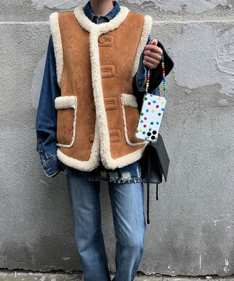 ブラウンとアイボリーのムートン風ベストをデニムジャケットとレイヤードし、濃淡デニムパンツと合わせたカジュアルな全身コーディネート。黒のショルダーバッグとカラフルなビーズのスマホストラップを合わせている。