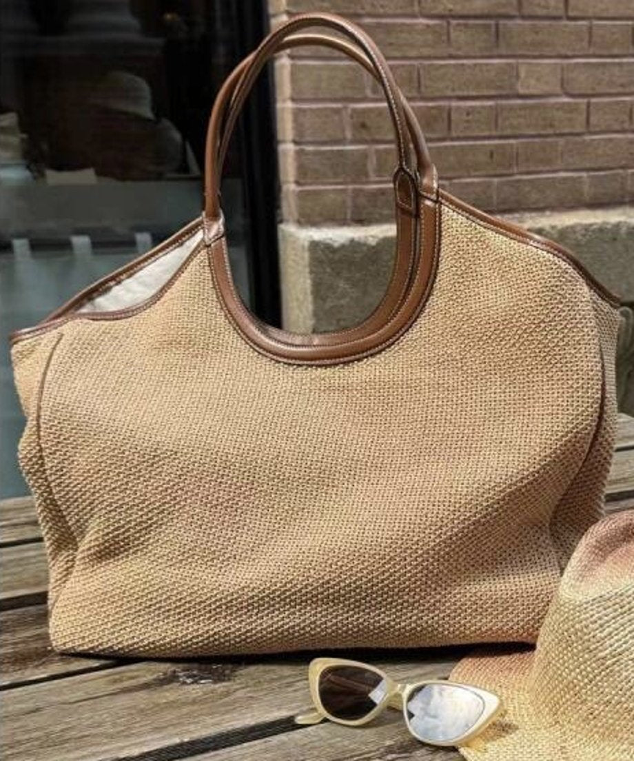 屋外のテーブルに置かれた編み込みトートバッグ、ブラウンの持ち手と縁取りがアクセントになっている。