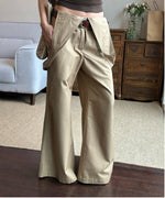 カーキのオーバーオールパンツをブラウンタンクトップと合わせた女性がベルトでウエストを締めたスタイル。
