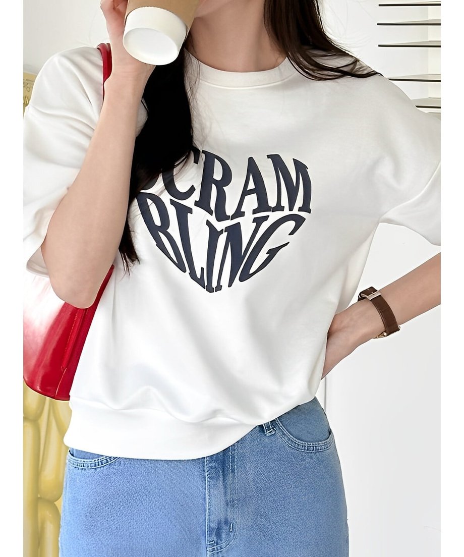 白いTシャツを着た女性がコーヒーカップを持っている様子。黒いロゴが前面にある。