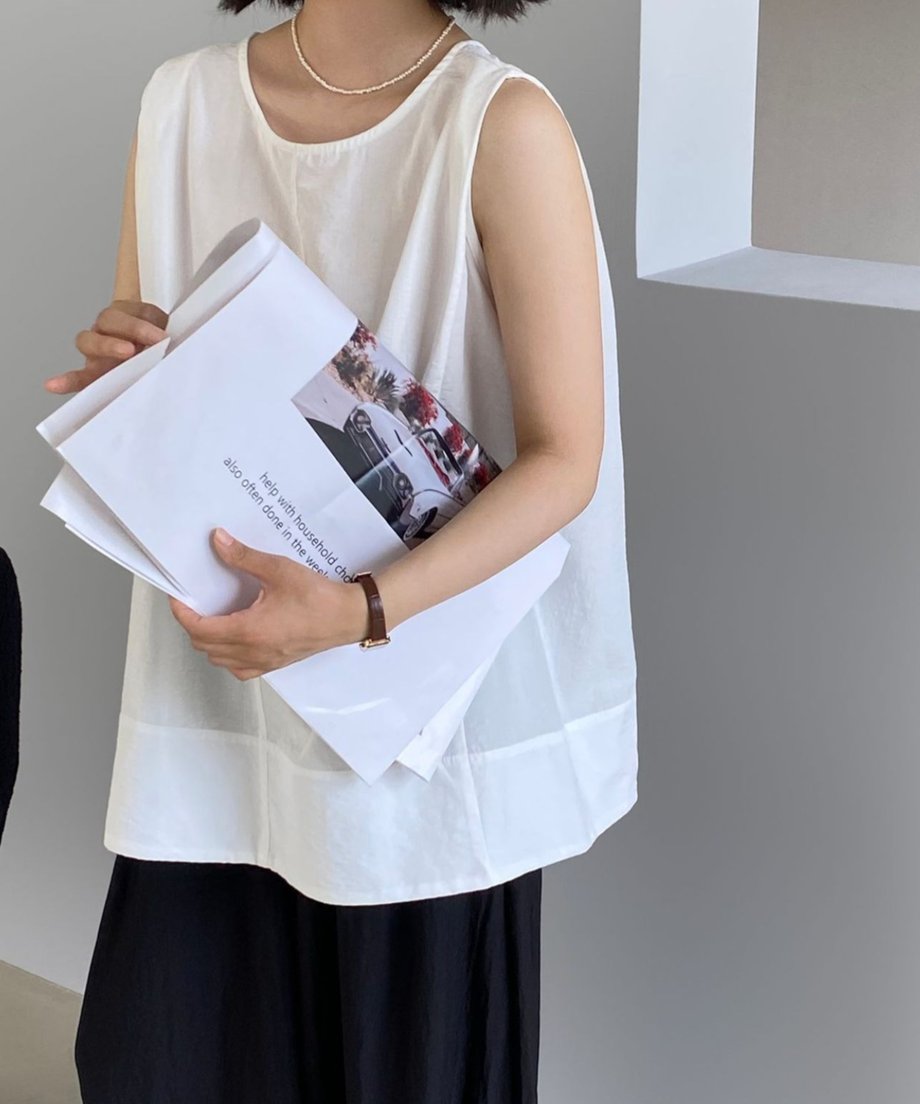 ホワイトブラウスを着た女性が手に新聞を持っている。