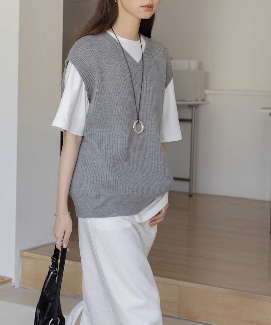 グレーのニットベストを着た女性が白いロングスカートと黒のバッグを持ったコーディネート。