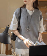 グレーのニットベストを着た女性が肩にバックをかけて立っている姿。