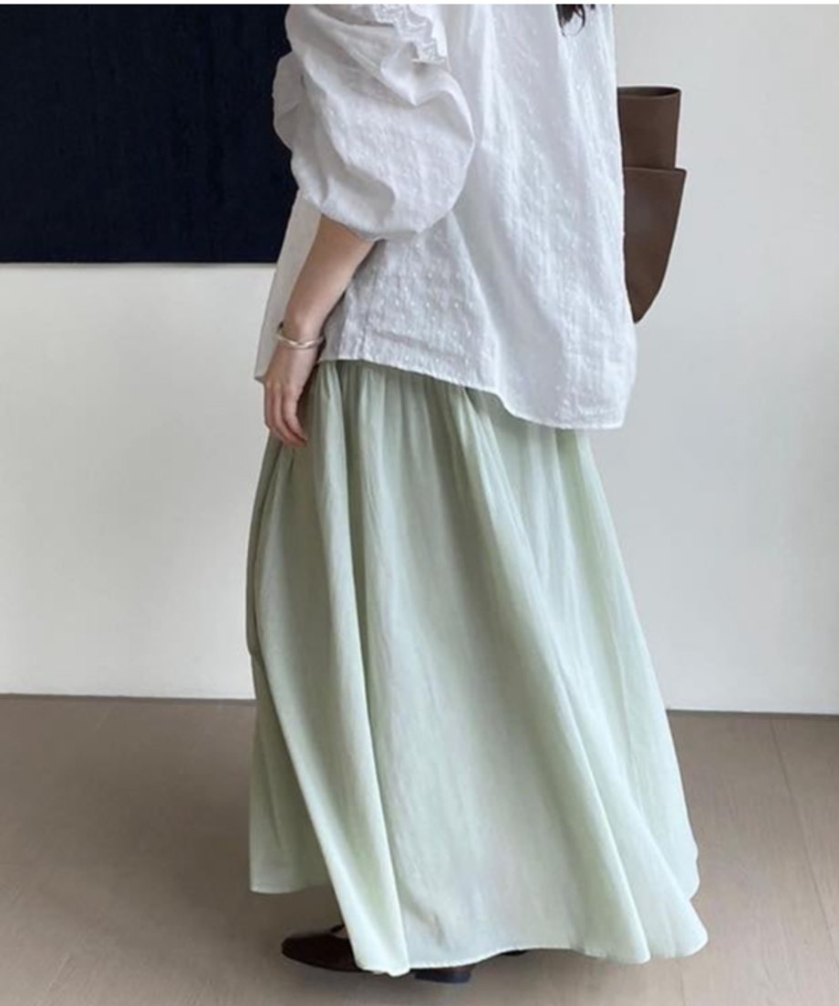 茶色のバッグを持ち、ミントグリーンのスカートを着用した女性の後姿。