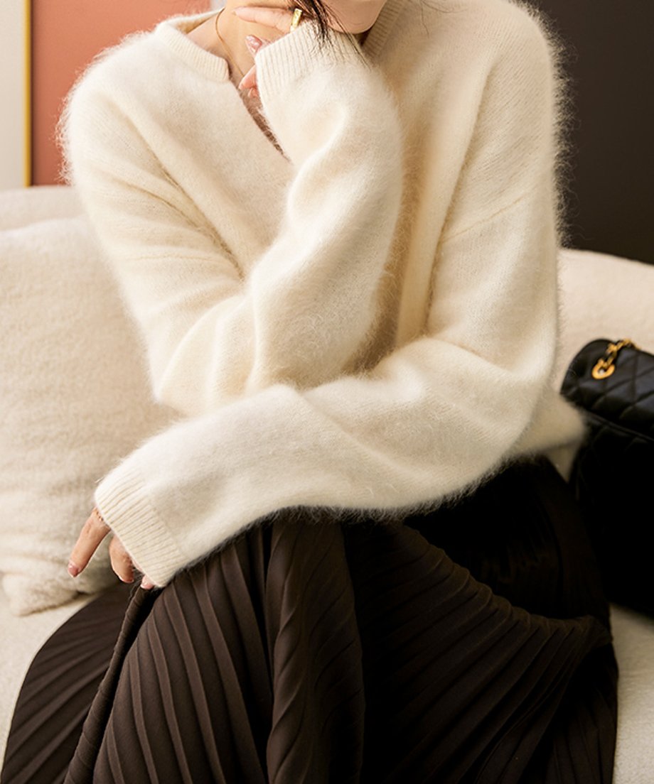 オフホワイトのセーターを着た女性が片手を頬に当て椅子に座っている様子。