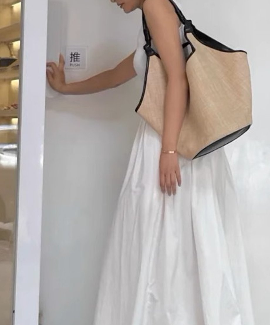 白いドレスを着た女性がベージュのトートバッグを肩にかけてドアを押している。