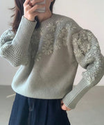 グリーンのフローラル刺繍セーターを着た女性、立体感のある編み込みの袖。