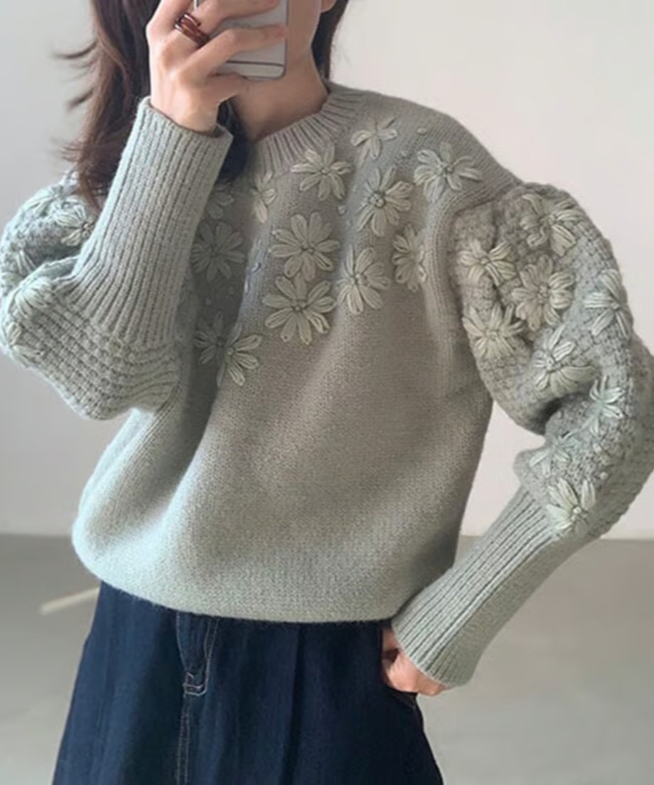 グリーンのフローラル刺繍セーターを着た女性、立体感のある編み込みの袖。