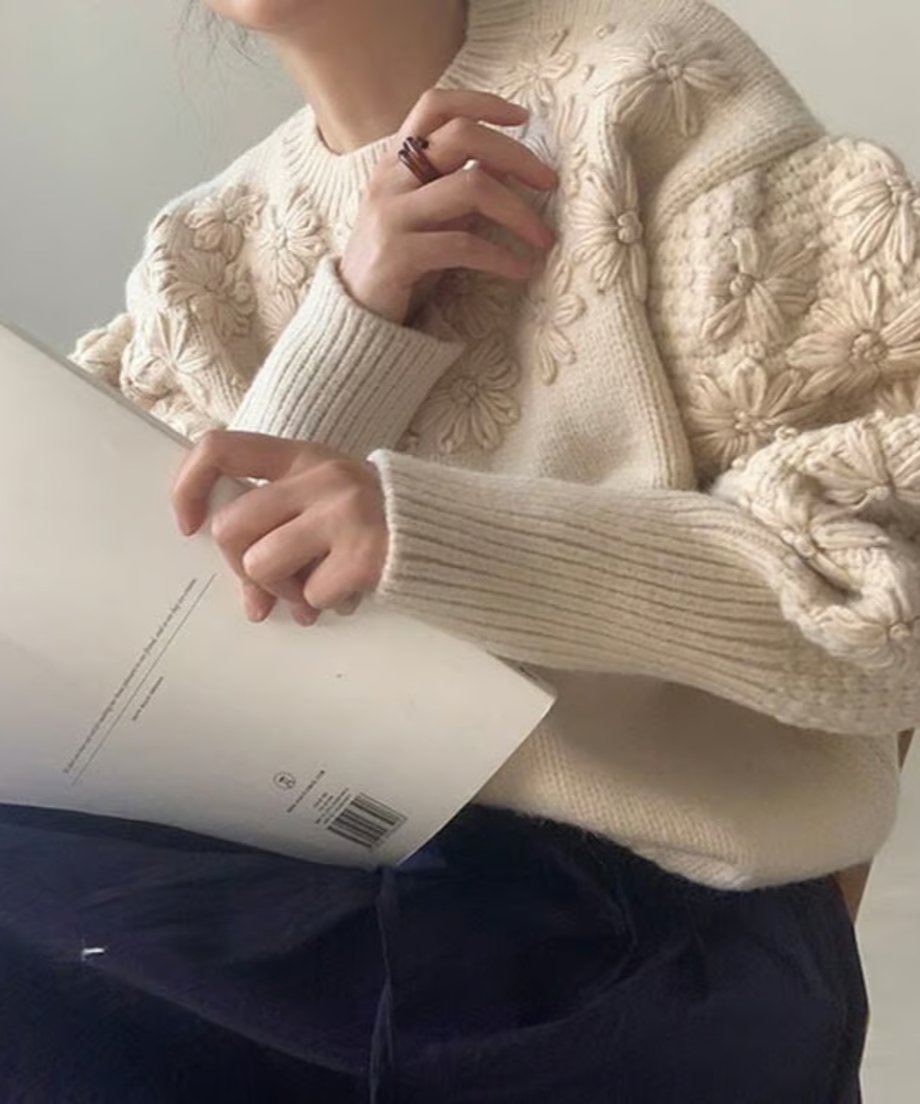 オフホワイトのフローラル刺繍セーターを着た女性が、リブ編みの袖口が特徴的なデザイン。