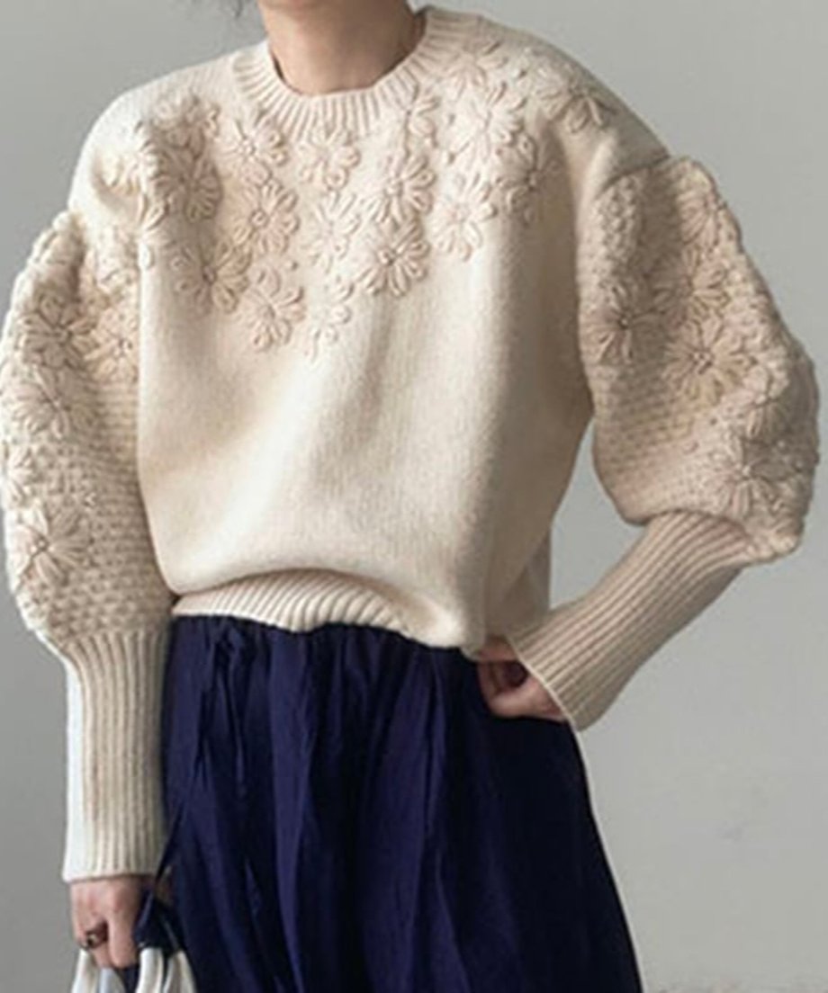 オフホワイトのフローラル刺繍セーターを着た女性、リブ編みのディテールが際立つデザイン。