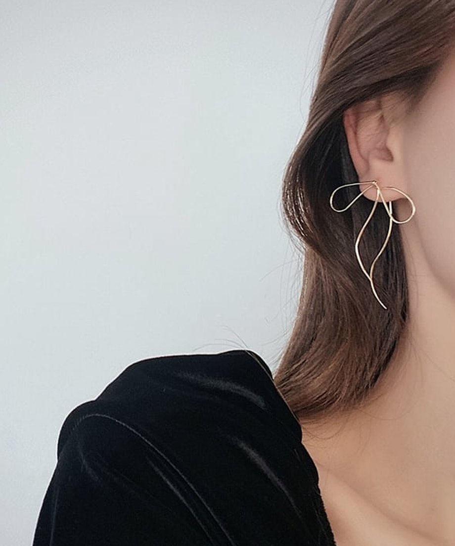 黒いトップスを着用した女性が、耳にゴールドのリボン型ピアスを付けている様子。