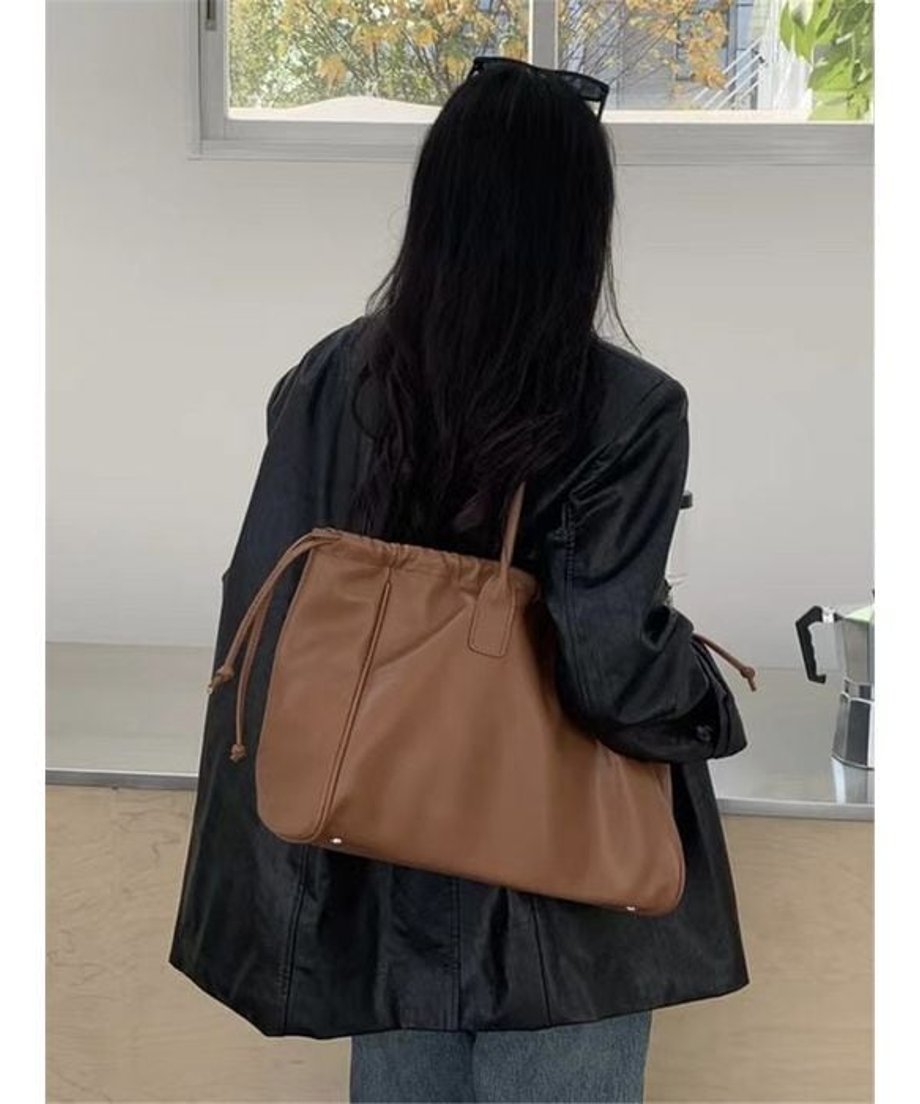 ブラウンのフェイクレザートートバッグを肩にかけている女性のアップ。レザージャケットとデニムを合わせたコーディネート。