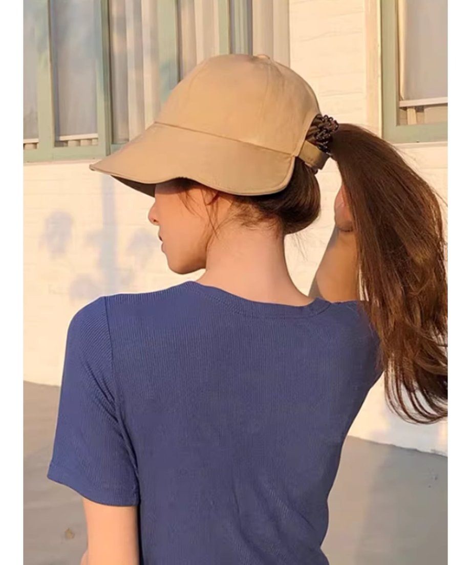 ベージュのつば広キャップをかぶり、紺色のリブトップスを着た女性の斜め後ろからの写真。結んだ髪をキャップの後ろ穴から出している。