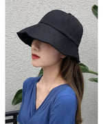 黒色のつば広キャップをかぶり、青いVネックのトップスを着た女性の横顔。髪は結ばずに下ろしている。