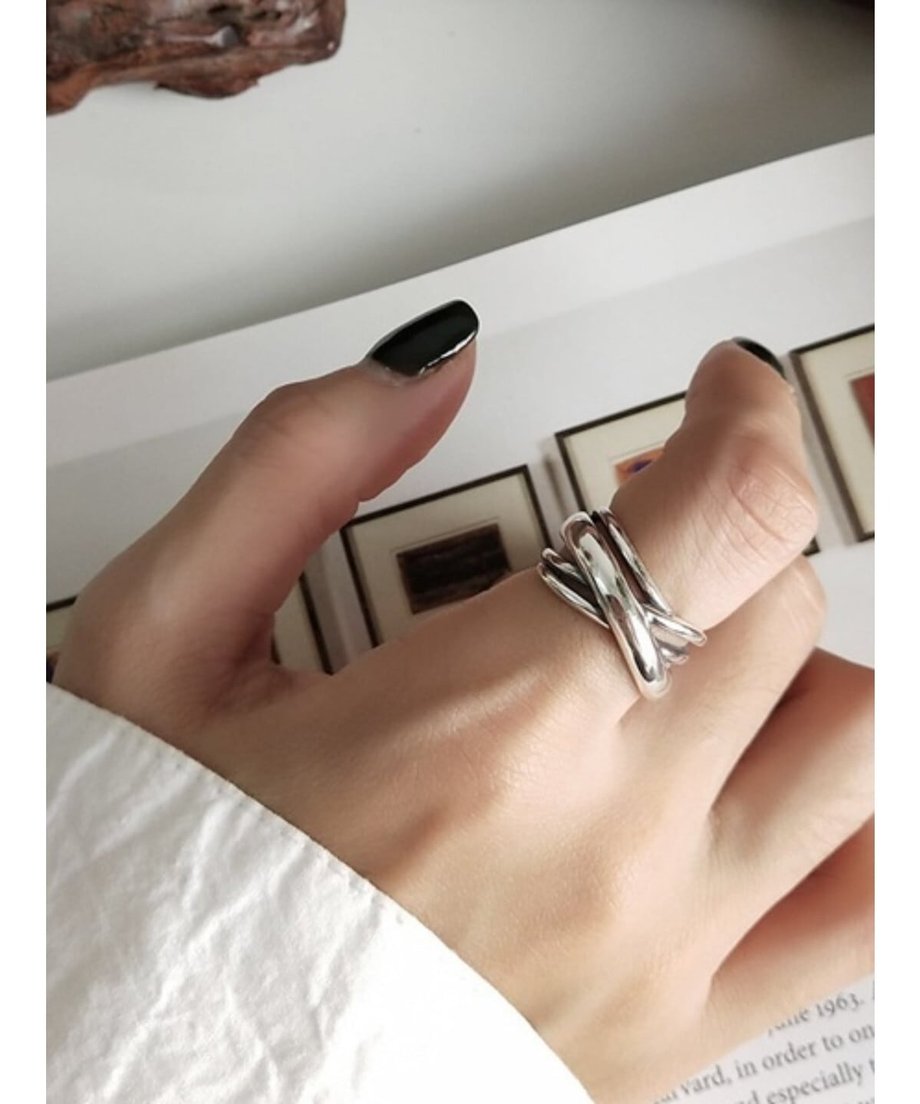 女性の指に着用された、なめらかな光沢を持つ幅広のクロスラインシルバーリング。黒いネイルがアクセント。