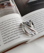 開いた雑誌の上に置かれた、光沢のあるクロスデザインのシルバーリング。内側に「S925」の刻印が見える。
