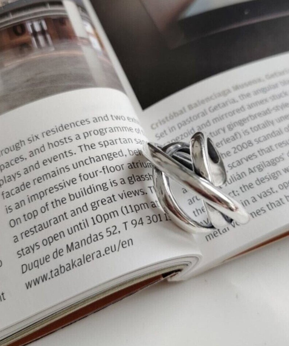 開いた雑誌の上に置かれた、光沢のあるクロスデザインのシルバーリング。内側に「S925」の刻印が見える。