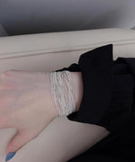 黒い袖の洋服に、繊細な多数のチェーンが束になったデザインのシルバーブレスレットを着用した女性の手首。