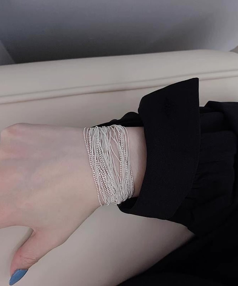 黒い袖の洋服に、繊細な多数のチェーンが束になったデザインのシルバーブレスレットを着用した女性の手首。