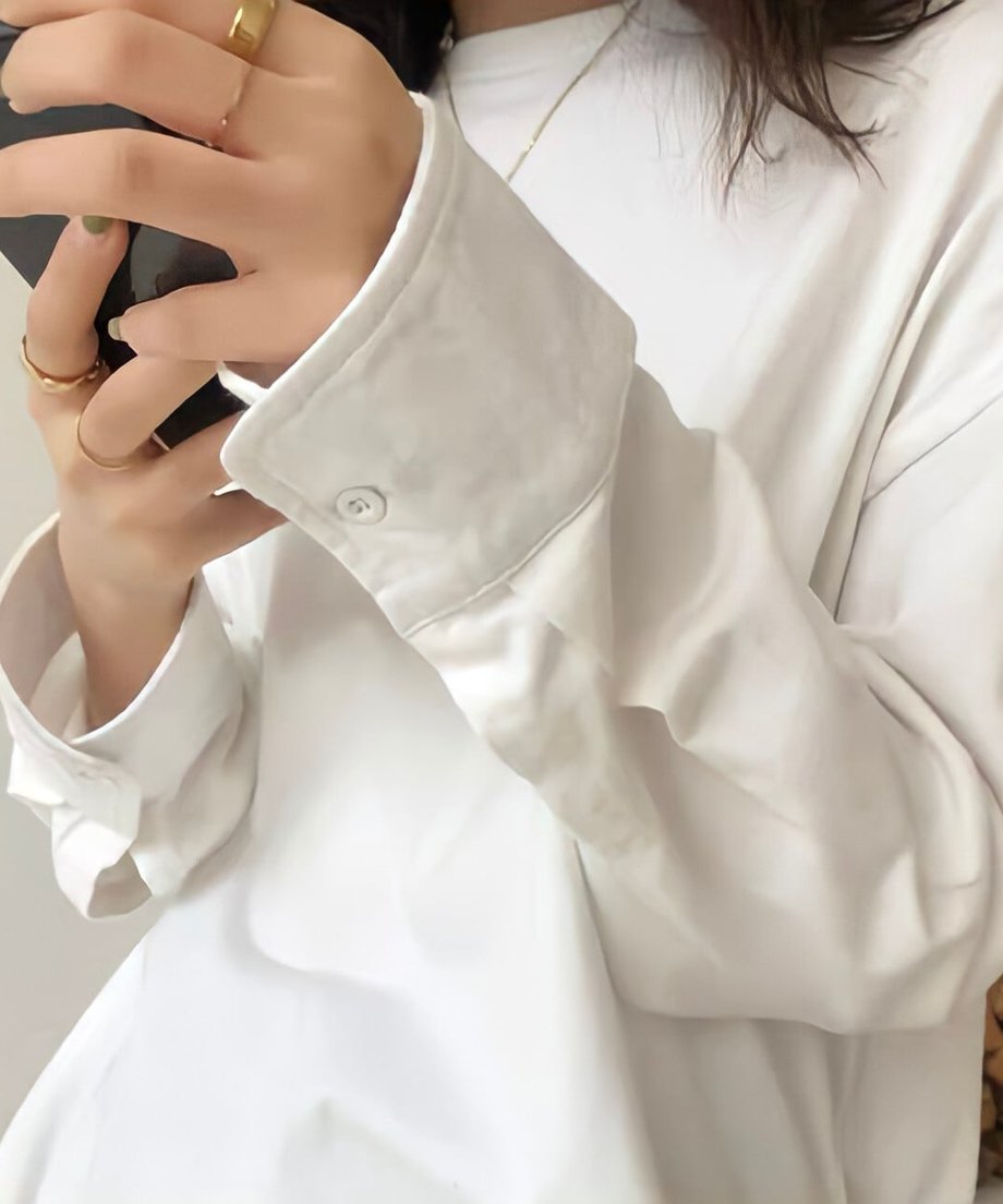 白のオーバーサイズ長袖Tシャツ（カットソー）を着用した女性のクロースアップ。ロング丈でゆったりとしたシルエットが特徴的で、アイスドリンクを持っている手元のディティールがよく見える写真